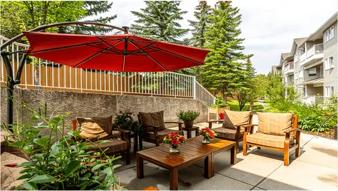 Patio seating beneath a red umbrella beside flowers and the residence
