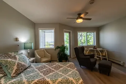 Room with a bed, two armchairs, a small table and windows