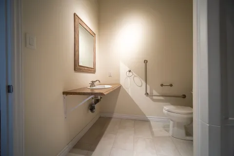Bathroom with a mirror, wall-mounted sink, toilet and grab bars