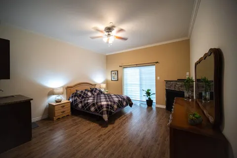 Bedroom with patterned bedding, a dresser, a ceiling fan and a stone fireplace