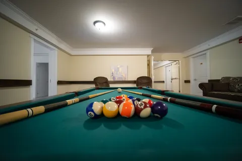Pool table with coloured balls and cues beside upholstered chairs