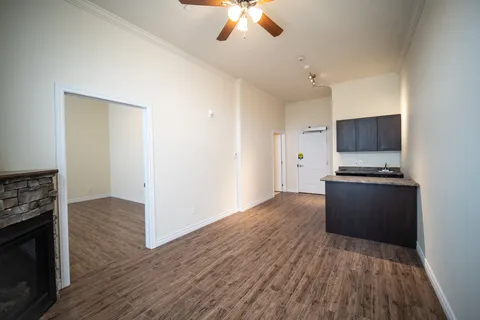 Unfurnished room with wood flooring, a kitchenette and a stone fireplace