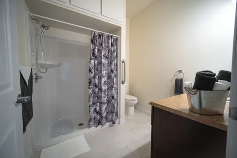 Bathroom with a walk-in shower, patterned curtain, toilet and folded towels