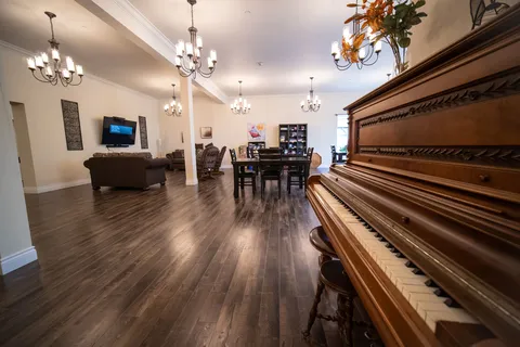 Room with an upright piano, chandeliers, armchairs, a television and tables