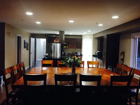 Wooden dining table and chairs beside a shared kitchen.