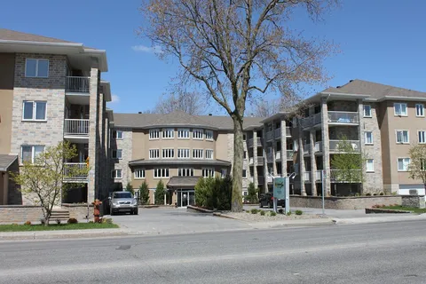 Residence buildings with balconies and a central entrance beside a large tree
