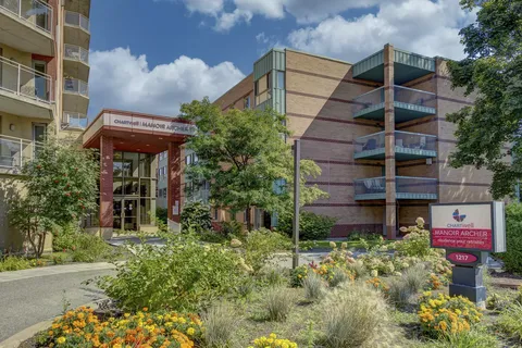 Brick residence with glass balconies, a covered entrance and landscaped flower beds