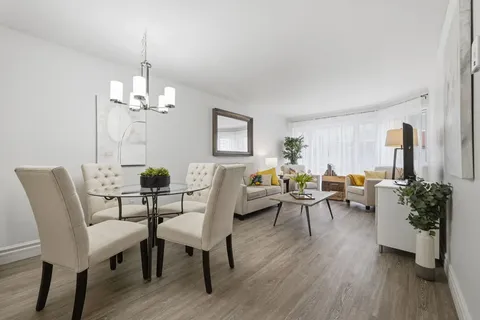 Living and dining area with cream chairs, a sofa, glass table and television