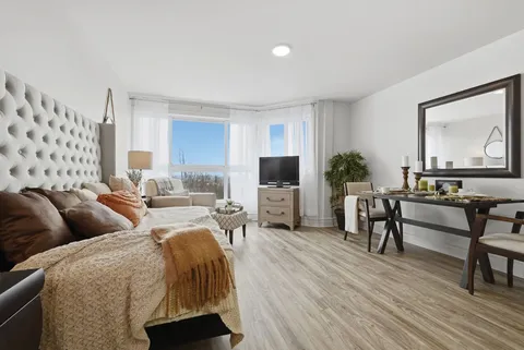 Room with a padded bed, dining table, television and large windows