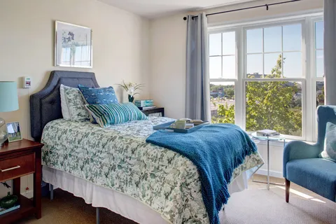 Bedroom with a bed, armchair, bedside table and large windows.
