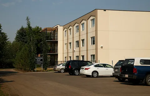 Side of a three-storey building with windows, parked cars and shrubs