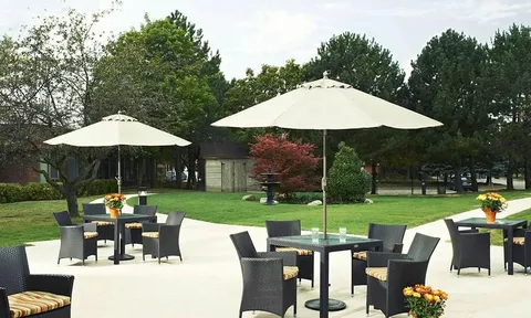 Patio dining tables with large umbrellas beside a lawn.