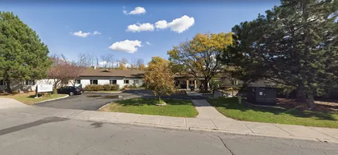 Single-storey building behind a curved driveway, lawn and trees