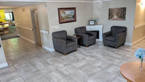 Three grey armchairs beside a white fireplace and framed landscape pictures