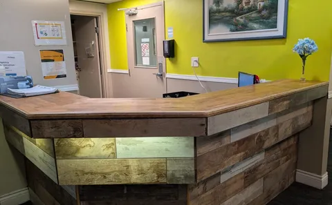 Wooden reception counter beside a green wall and framed landscape painting