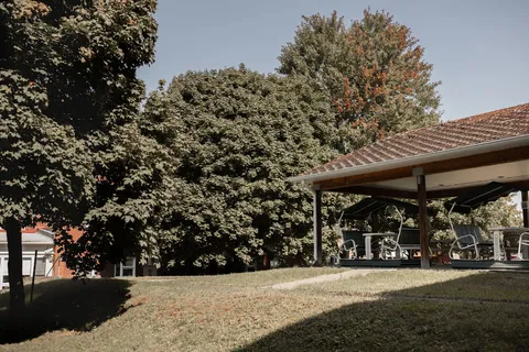 Covered patio seating beside a lawn, trees and the residence