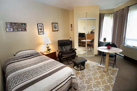 Bedroom with a bed, armchair, small table and large windows.