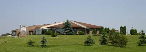 Residence exterior on a grassy slope with trees and an entrance driveway.