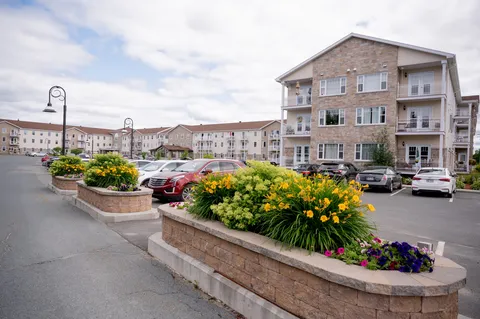 Three-storey residence with stone-faced sections, balconies, parked cars and raised flower beds