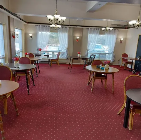 Dining room with round tables, red chairs, chandeliers and curtained windows