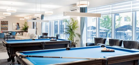 Bright room with blue-felt billiard tables and seating beside large windows