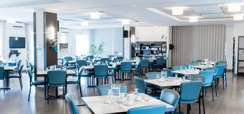 Dining room with blue chairs and tables set with glasses and napkins