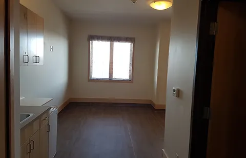 Empty room with a kitchenette, wooden cupboards and a window