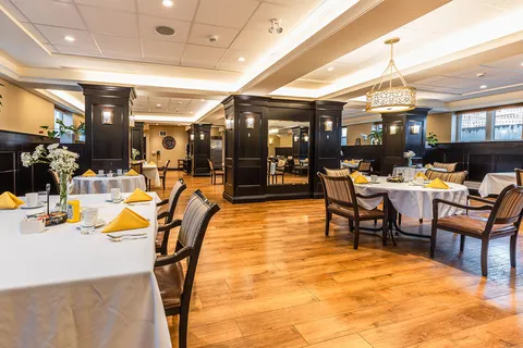 Dining room with white-covered tables, wooden chairs and yellow folded napkins
