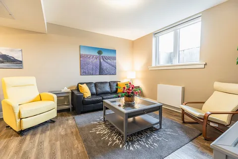 Room with a black sofa, two armchairs, a glass coffee table and landscape prints