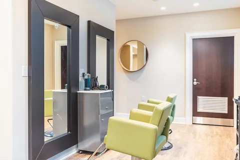 Salon with two green chairs, tall mirrors and a metal storage cabinet