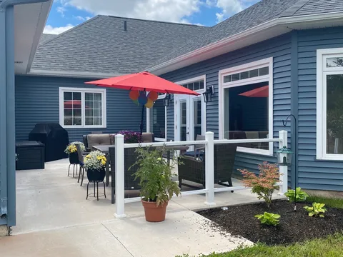 Blue-sided building surrounding a patio with a red umbrella, wicker seating and flower pots