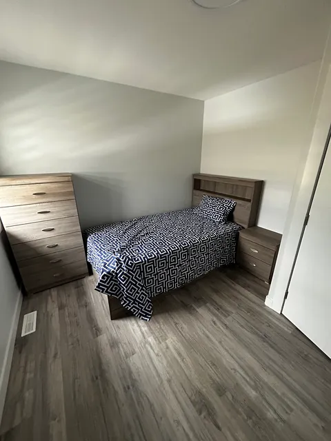 Bedroom with a blue patterned bedspread, wooden drawers and a white closet.