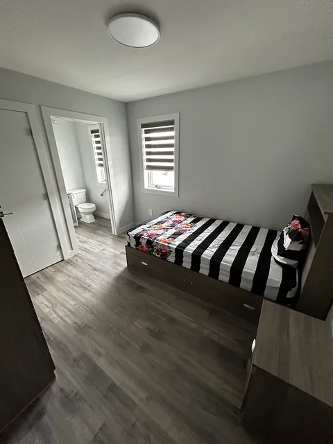 Bedroom with a striped floral bedspread and an open door to a bathroom.
