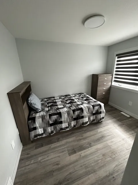 Bedroom with a checked bedspread, a wooden chest of drawers and a window.