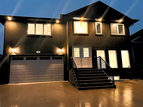 Two-storey dark-sided residence with a garage and front steps illuminated at dusk.