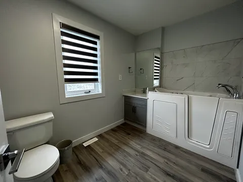 Bathroom with a walk-in bathtub, toilet, sink and a window.