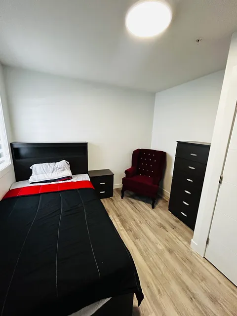 Bedroom with a black and red bedspread, a red chair and dark drawers.