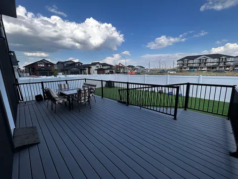 Raised deck with a table, cushioned chairs and black railings above a fenced lawn.