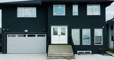 Dark-sided residence facade with white double doors, front steps and a garage.