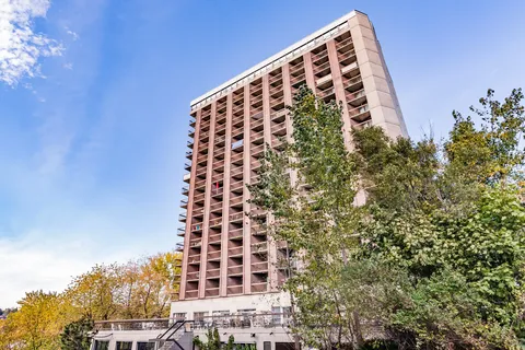 Tall residence tower with balconies, trees and a covered ground-floor frontage.