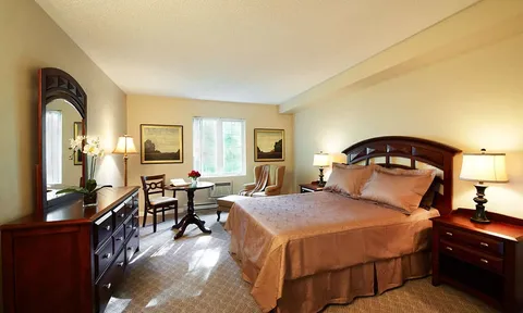 Bedroom with a double bed, dark wood furniture, lamps, a round table and two chairs