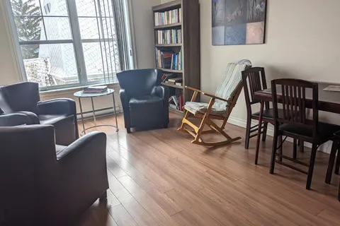 Room with black armchairs, a wooden rocking chair and a bookshelf