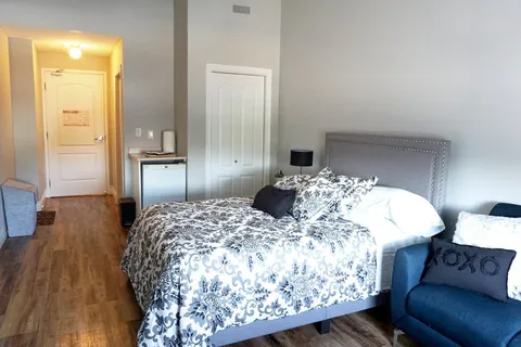 Bedroom with a bed, armchair and refrigerator beside the entrance