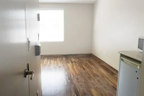 Unfurnished room with wood flooring, a window and a kitchenette