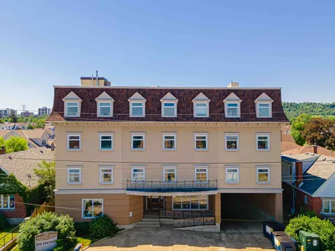 Four-storey residence with dormer windows and trees beside the entrance