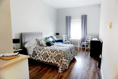 Bedroom with a bed, armchair, dining table and window