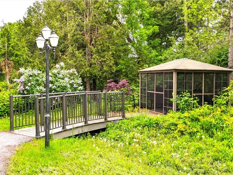 Wooden bridge leading to a gazebo amid trees and greenery