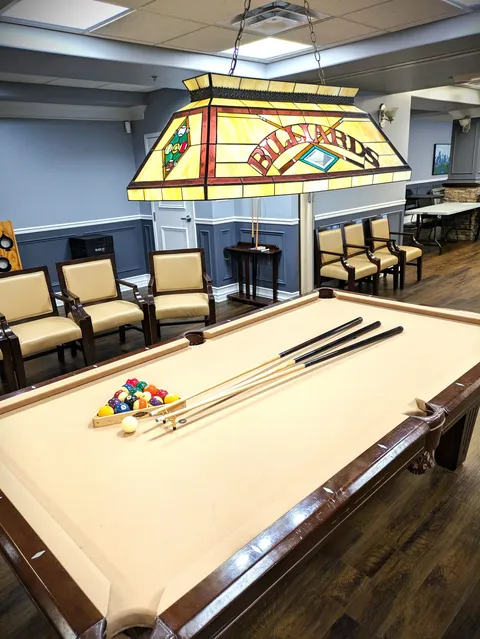 Billiard table beneath a stained-glass lamp with chairs around the room