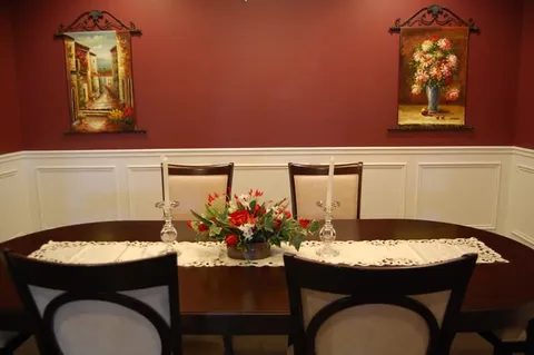 Dining table with chairs, a floral arrangement and pictures on a red wall