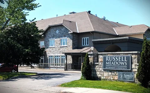 Stone-fronted residence with large windows, driveway and a sign beside the lawn